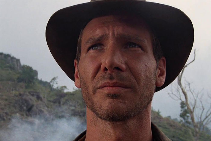 Actor in rugged costume, wearing a hat, embodying a role flawlessly in a dramatic outdoor setting.