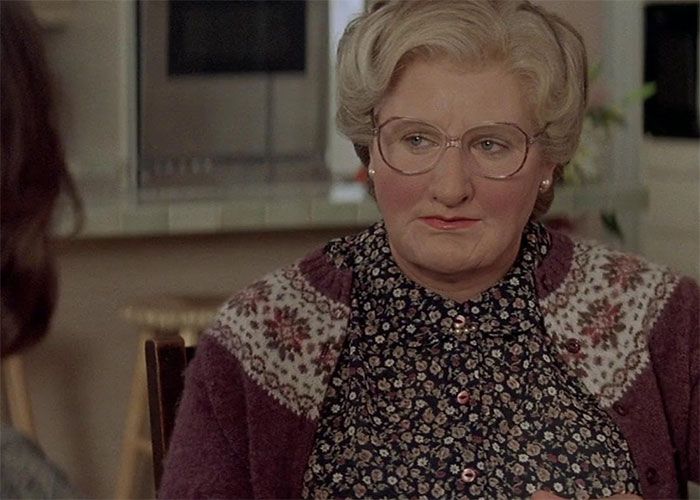 An actor in a floral outfit and glasses, embodying a role flawlessly in a kitchen setting.