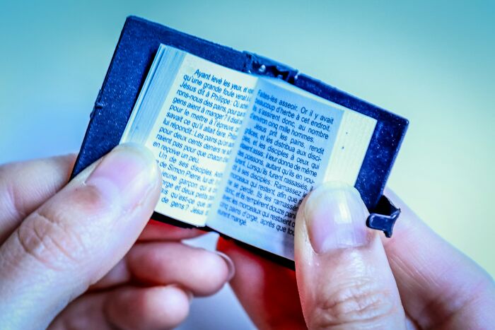 Close-up of hands holding a tiny open book with text, representing something small succeeding despite being outnumbered.