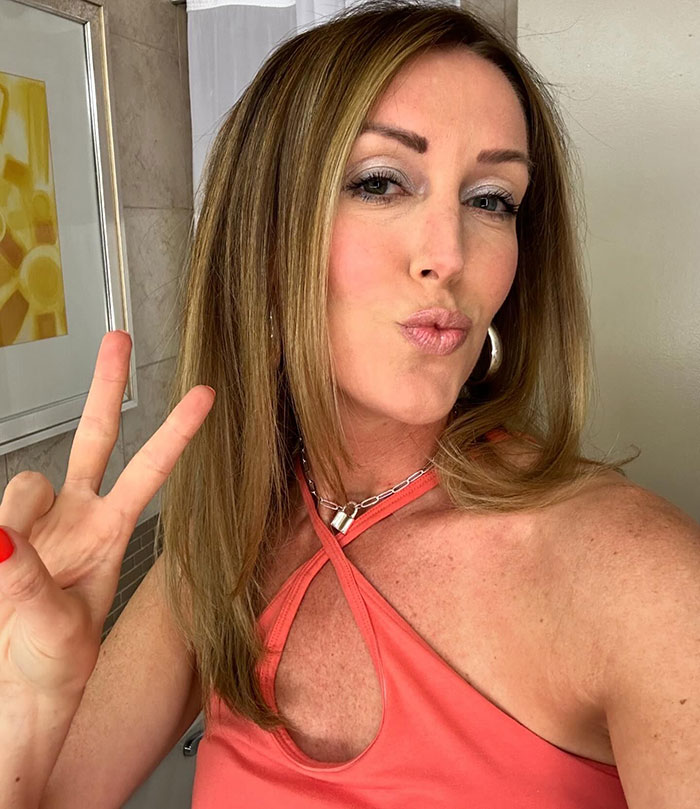 Selfie of a woman in a coral top making a peace sign, related to tattoo trends among young people.