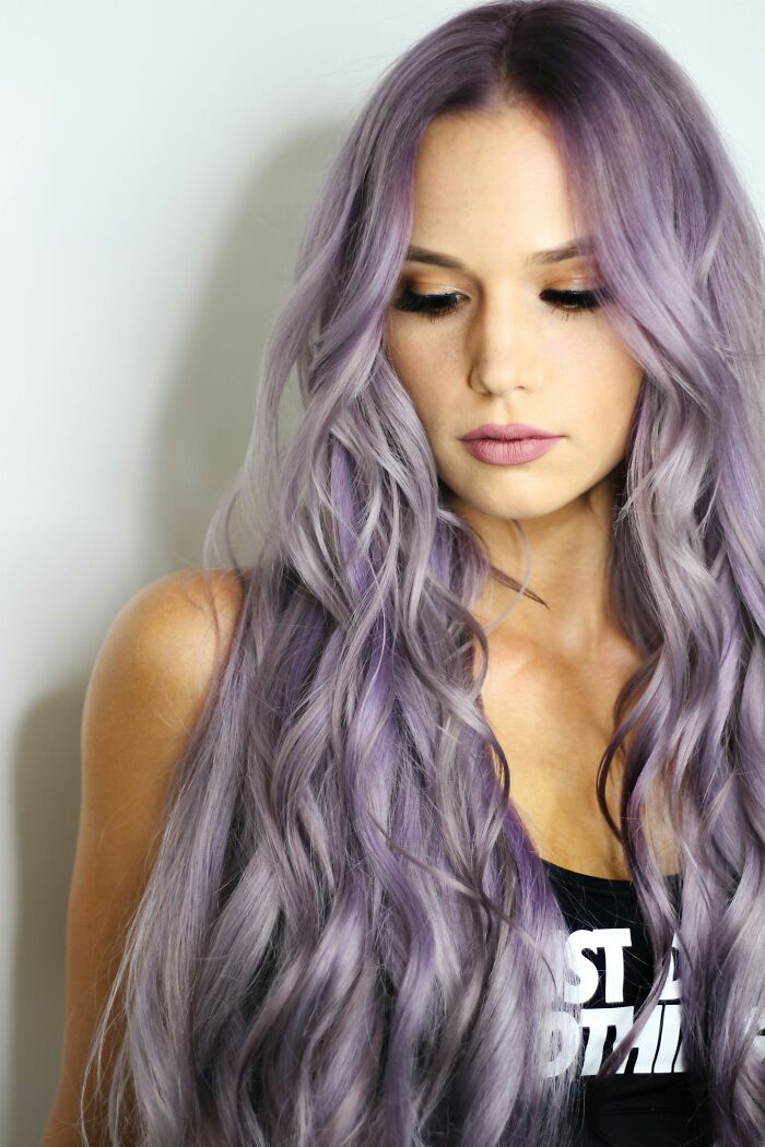 Woman with long lavender hair looking down, wearing a black top, illustrating individuality and style.
