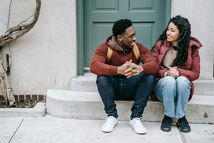 Two adults practicing life skills through conversation, sitting on steps in casual attire.