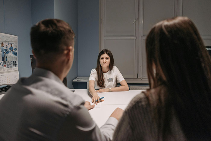 Three adults in a meeting room discussing essential life skills over a table.