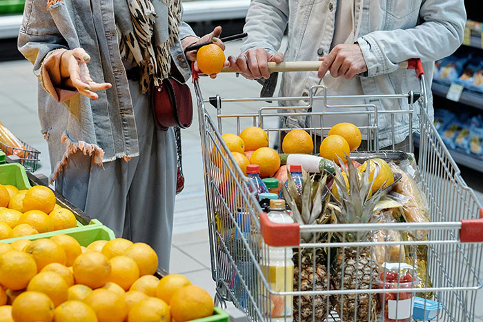 Two adults shopping for groceries, selecting oranges and pineapples, demonstrating essential life skills.