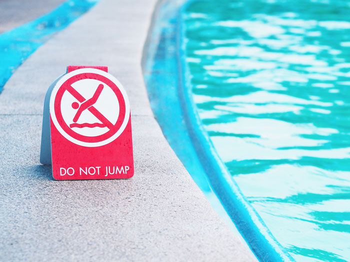 Safety sign by a pool edge with "Do Not Jump," highlighting safety concerns. Safety sign by a pool edge with "Do Not Jump," highlighting safety concerns.