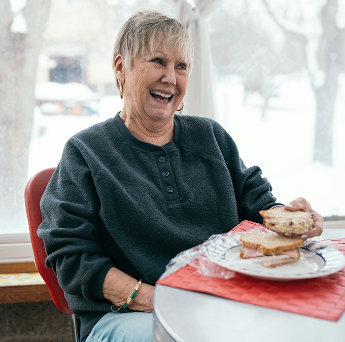 Smiling elderly woman enjoying a meal, showcasing a family setting.