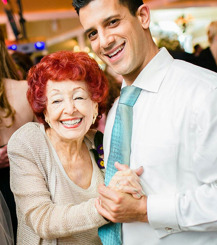 A man smiling as he dances with an elderly woman, both looking happy and enjoying the moment together.