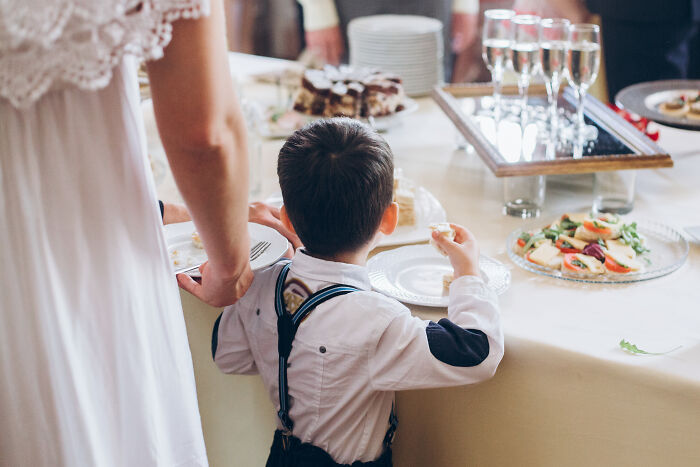 Child in formal attire at a wedding reception table with appetizers and champagne.