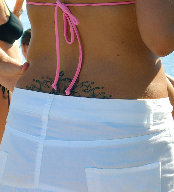 Lower back tattoo with a sea-themed design, visible above white shorts, representing 2024 tattoo trends among youth.