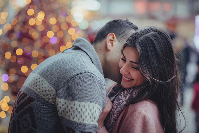 Couple embracing in front of festive lights, capturing a moment of romance during a holiday season.