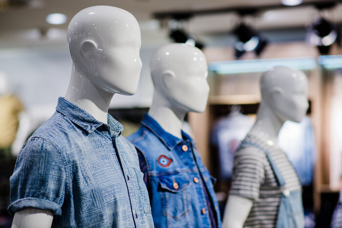 Mannequins in casual denim and striped shirts displayed in a brightly lit clothing store.