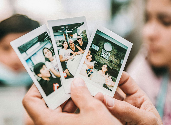 Close-up of hands holding three Polaroid photos, depicting casual moments in an indoor setting, linked to Hollywood secrets.