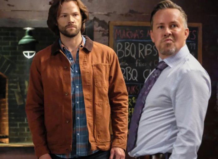 Two men in a bar, one wearing a brown jacket, the other in a tie; capturing Hollywood's entertainment industry scene.