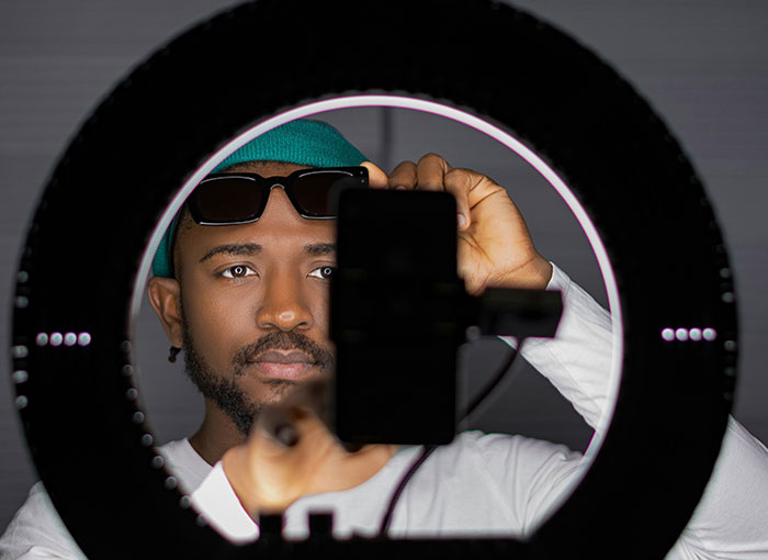 Man behind a light ring with a smartphone, revealing secrets about Hollywood.