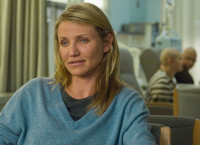 Woman in a blue sweater sitting in a room, conveying emotions related to Hollywood secrets.