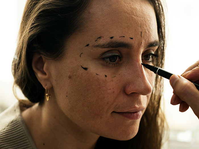 Woman with cosmetic markings on her face, highlighting Hollywood's dark secrets in the entertainment industry.