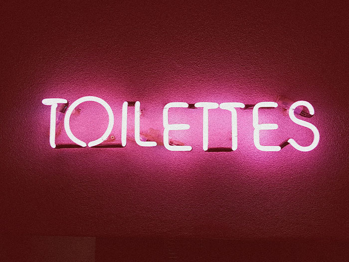 Neon "Toilettes" sign glowing pink in low-light ambiance, related to Hollywood entertainment secrets.