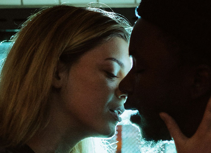 Two people sharing an intimate moment under moody lighting, hinting at Hollywood's entertainment industry secrets.