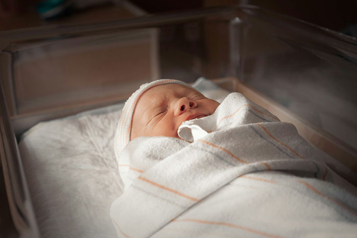 Newborn baby wrapped in a blanket, peacefully sleeping in a hospital bassinet.