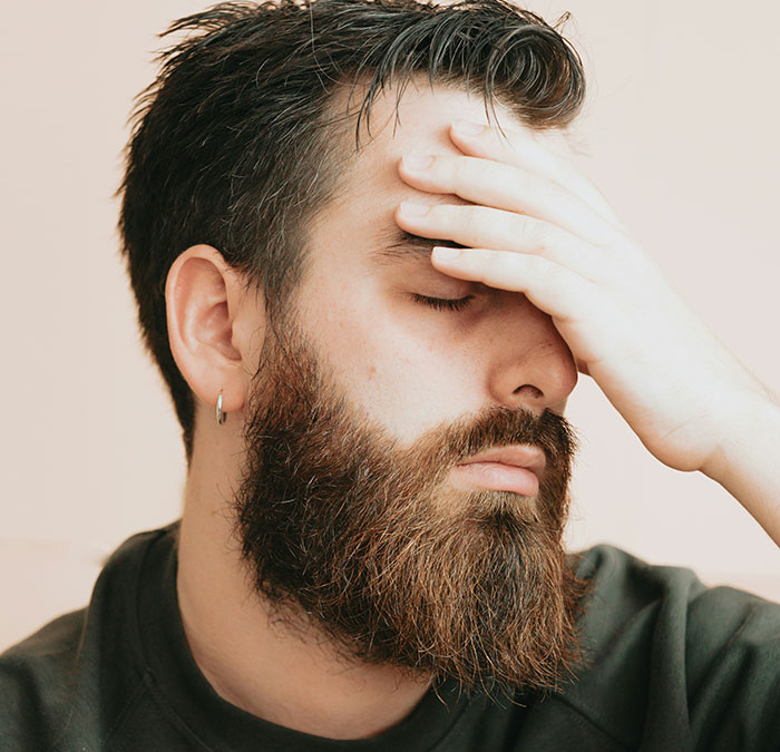 Man with a beard looking frustrated, hand on forehead, reflecting family tension over child's arrival.