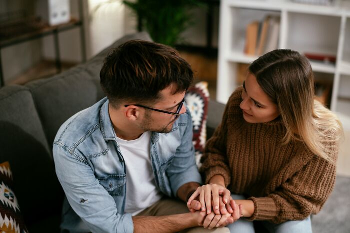 A couple on a couch holding hands, conveying emotions related to family dynamics and relationship challenges.