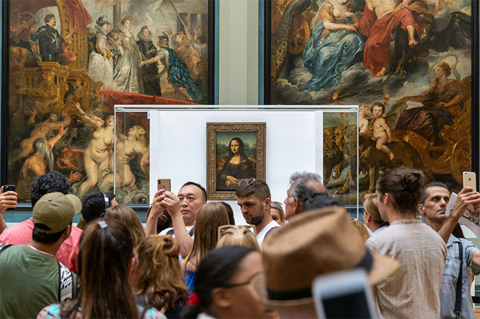 Crowded museum visitors photographing the Mona Lisa, highlighting hyped travel destinations that can disappoint.