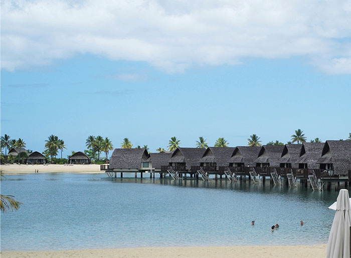 Overwater bungalows on a tropical beach with palm trees, viewed as a hyped travel destination.