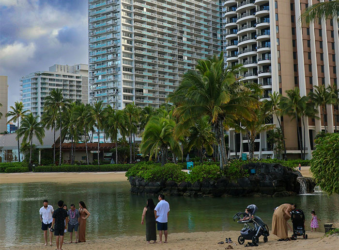People gathered at a tropical beach with tall buildings and palm trees, discussing hyped travel destinations.