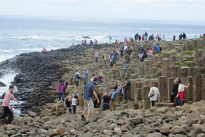 Crowded tourist destination with people walking on rocky columns by the sea.