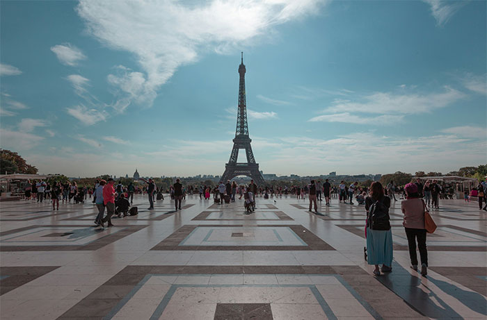 Eiffel Tower standing tall under a cloudy sky, surrounded by tourists on a wide plaza.