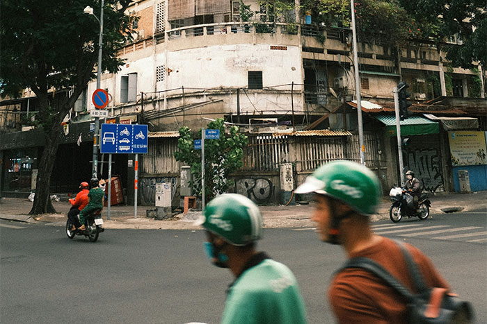 Street with motorcyclists passing by a run-down building in a hyped travel destination.