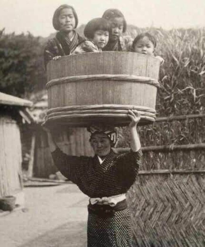Una mujer japonesa lleva a sus hijos en un cubo sobre la cabeza, Japón, 1900