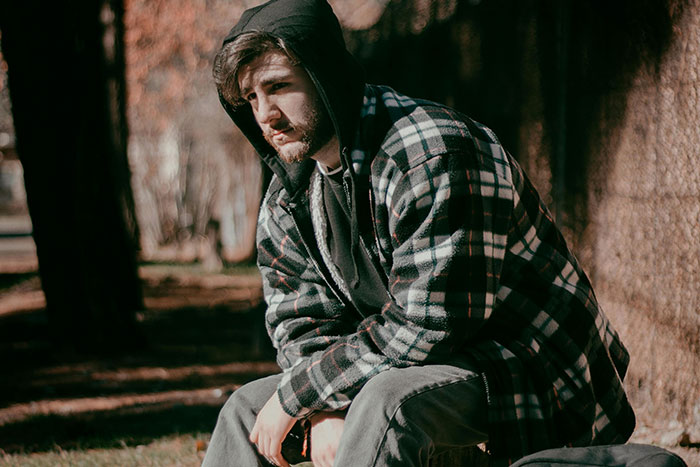 A man in a checkered jacket sits thoughtfully in an outdoor setting, embodying the solitude of being a senior.