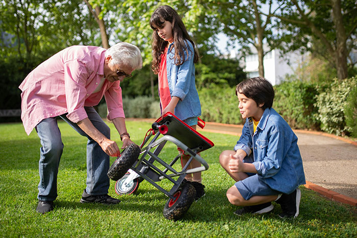 Senior with two children fixing a wheelbarrow in a garden, illustrating active senior lifestyles.