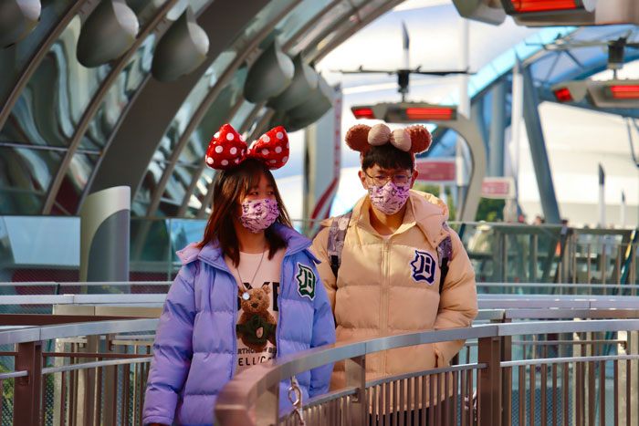 Two people wearing matching face masks and Disney-themed costumes walking on a futuristic path. Two people wearing matching face masks and Disney-themed costumes walking on a futuristic path.