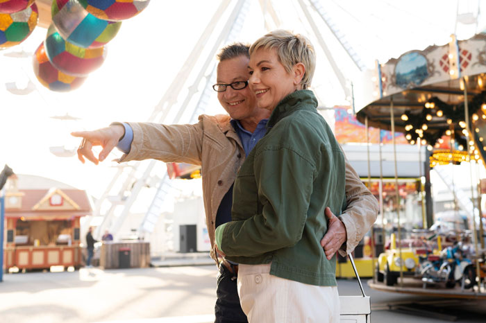 A couple enjoying a date at an amusement park, with colorful balloons and a Ferris wheel in the background. A couple enjoying a date at an amusement park, with colorful balloons and a Ferris wheel in the background.