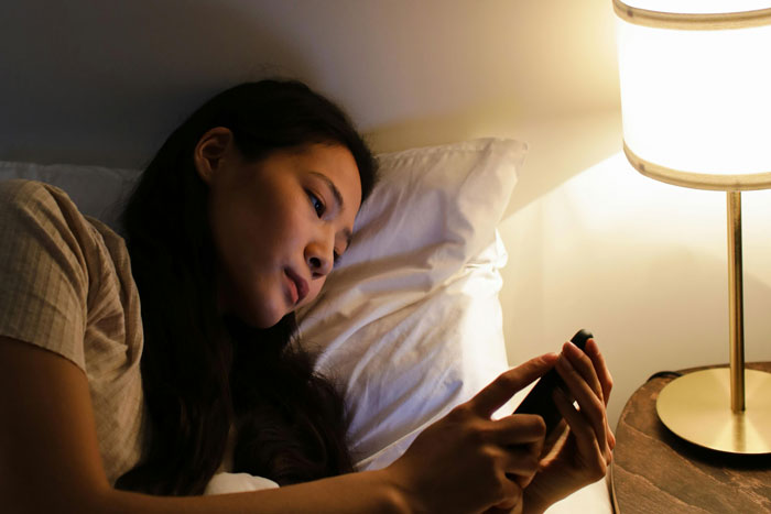 A person lying in bed, looking at their phone, illuminated by a bedside lamp, conveying a sense of being stalked. A person lying in bed, looking at their phone, illuminated by a bedside lamp, conveying a sense of being stalked.