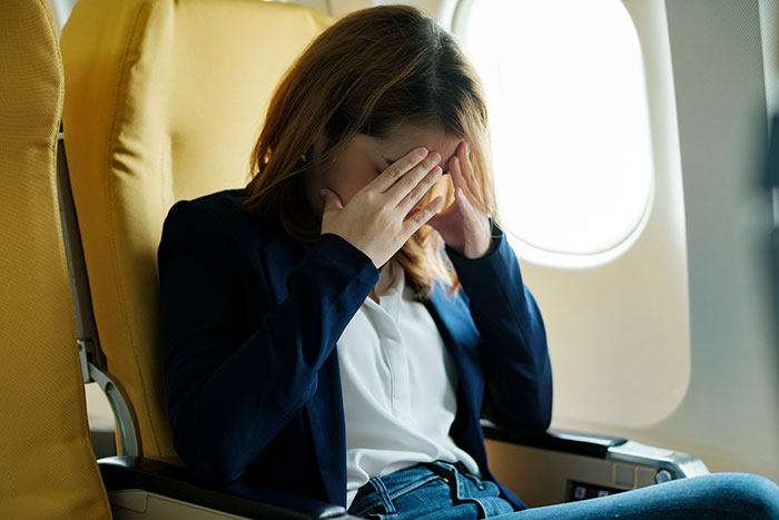 A woman in an airplane seat holding her face in distress, related to a failed attempt to switch seats.