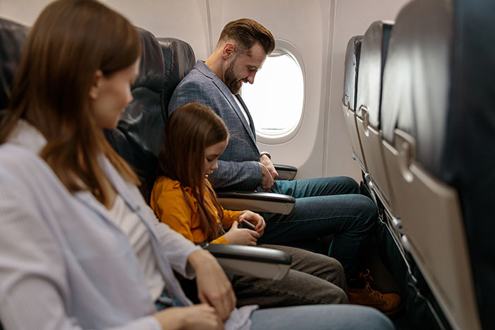 Family sitting together in airplane seats, looking down with thoughtful expressions.