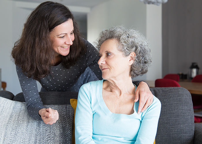 Young woman and older woman smiling on a couch, discussing life realities shared by people in their 40s.