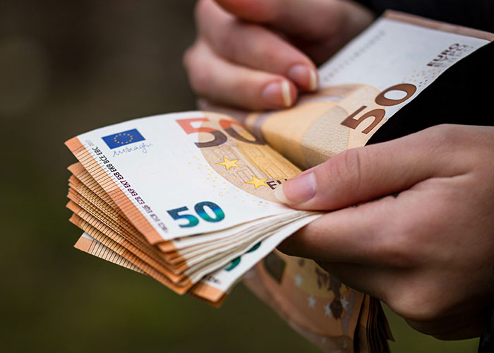Hands holding a stack of 50 euro notes, representing harsh life realities about money management in your 20s.