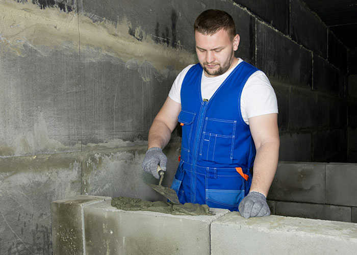 A man in a blue vest lays bricks, illustrating realistic life skills for 20-somethings.