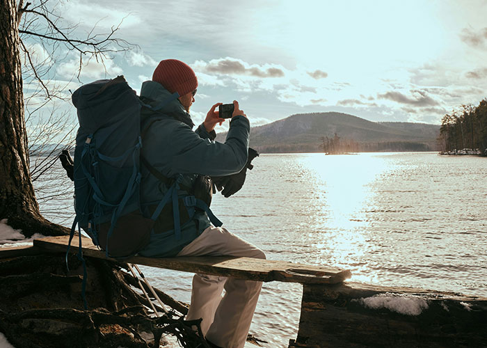 A person in their 20s takes a photo of a scenic lake view, unaware of life realities discussed by people in their 40s.