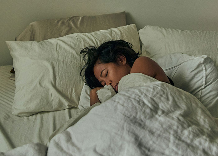 Young woman asleep in bed, illustrating harsh life realities often unrecognized by 20-somethings.