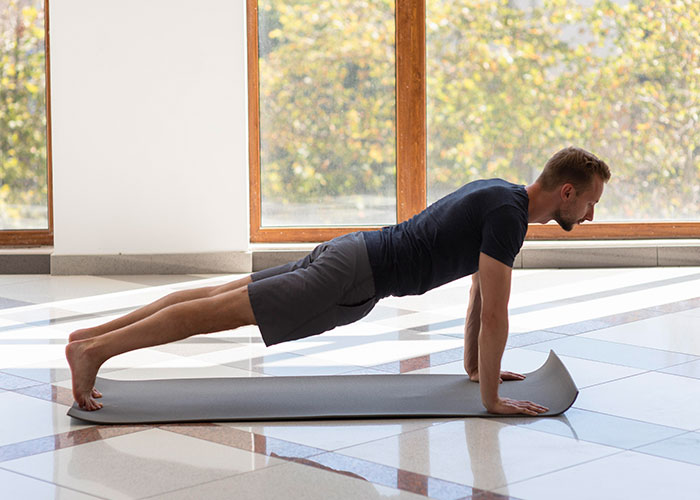 Man in plank pose on yoga mat in bright room, embodying life realities for 20-somethings.