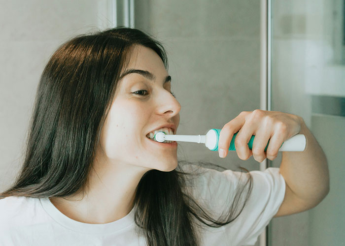 Young woman brushing teeth with electric toothbrush, focusing on health, one of the life realities for 20-somethings.