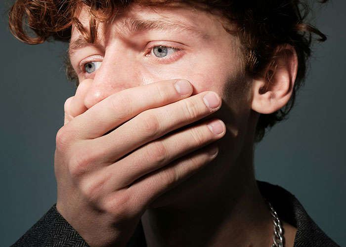 Young man with hand over mouth, contemplating harsh life realities.