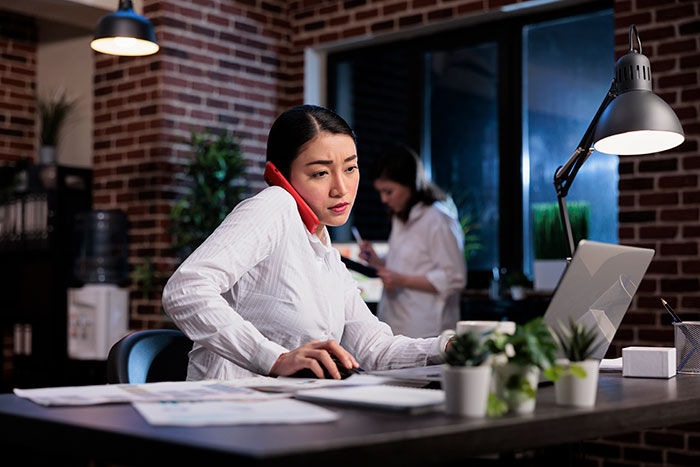 Person in a busy office setting, multitasking with a phone and laptop, highlighting job in finance.