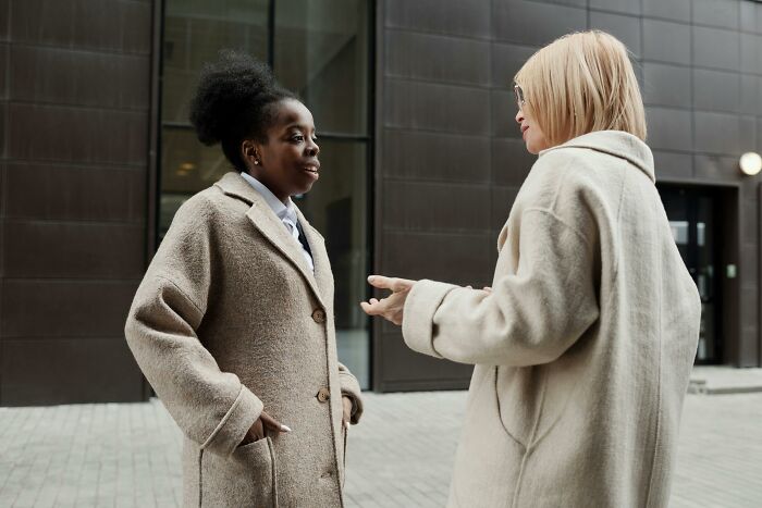 Two people in beige coats talking outside a building, illustrating conversational dynamics.