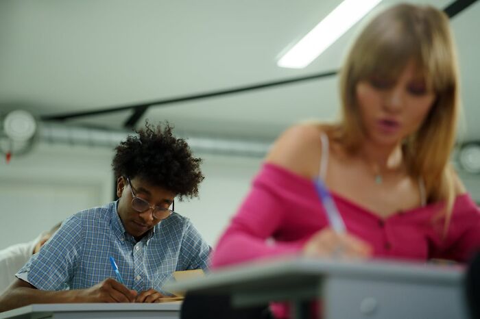 Two students writing at desks in a classroom setting, focused and intent.